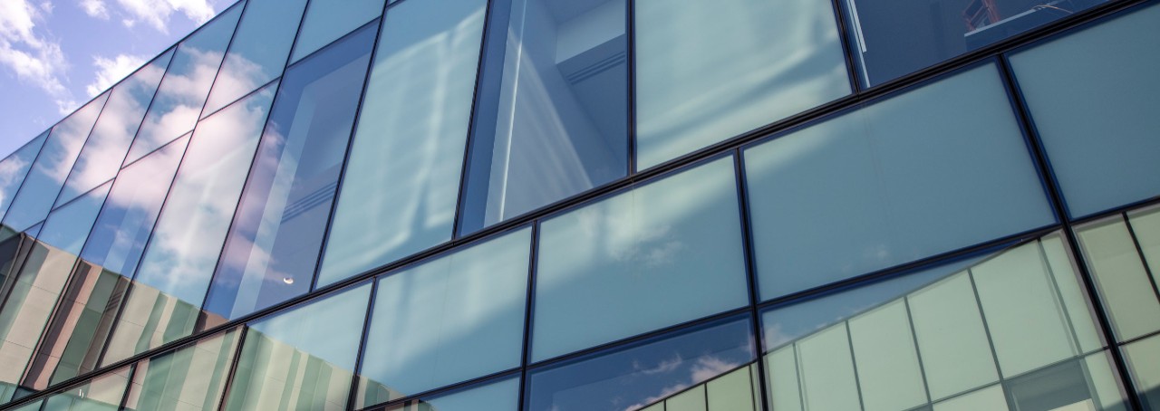artistic shot of part of the wall in the interior courtyard at Carl H. Lindner Hall, with green reflective glass and part of the sky in the top lefthand corner