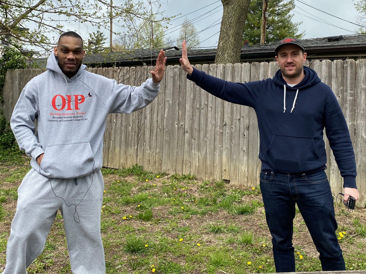 a man in a grey sweatshirt and jogging pants gives a high five from a distance to a man in a blue hoodie and jeans