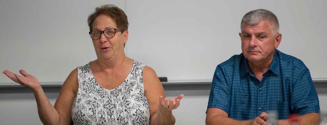 a woman wearing a tank top and a man wearing a short sleeve blue shirt site at a table