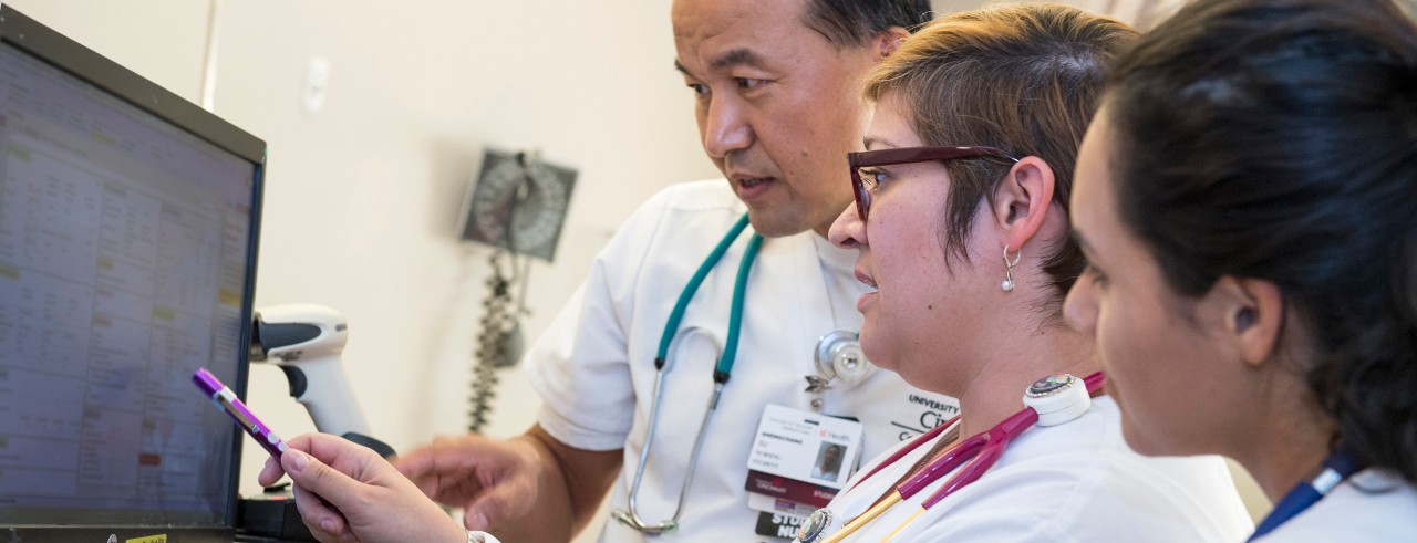 Two nursing students look at a computer screen showing medical information with an instructor