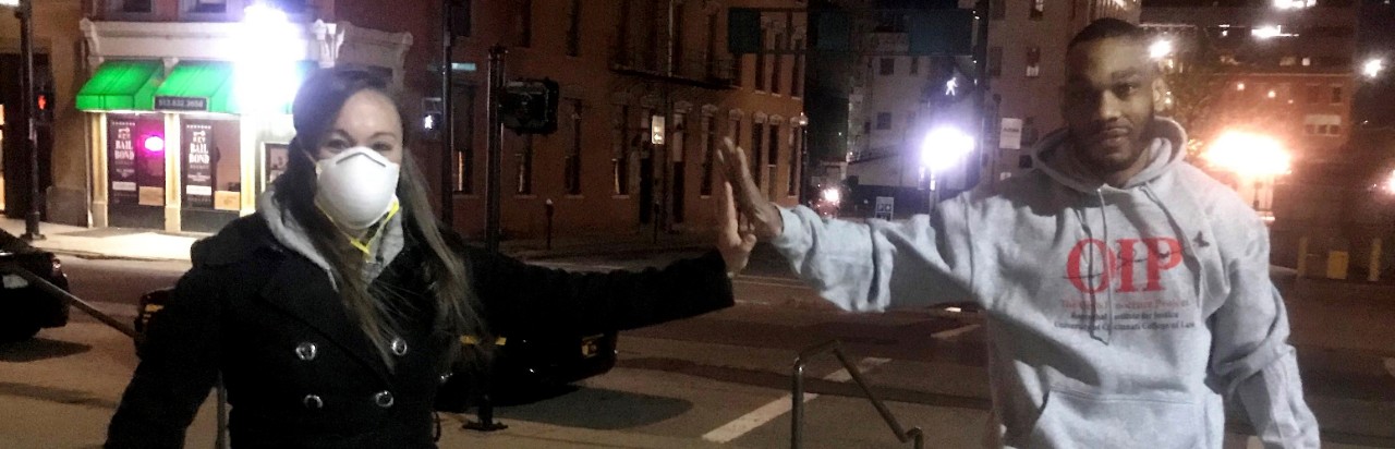 A man in a grey sweatshirt and maroon jogging pants gives a high five at a distance to a woman wearing the same grey sweatshirt and maroon leggings