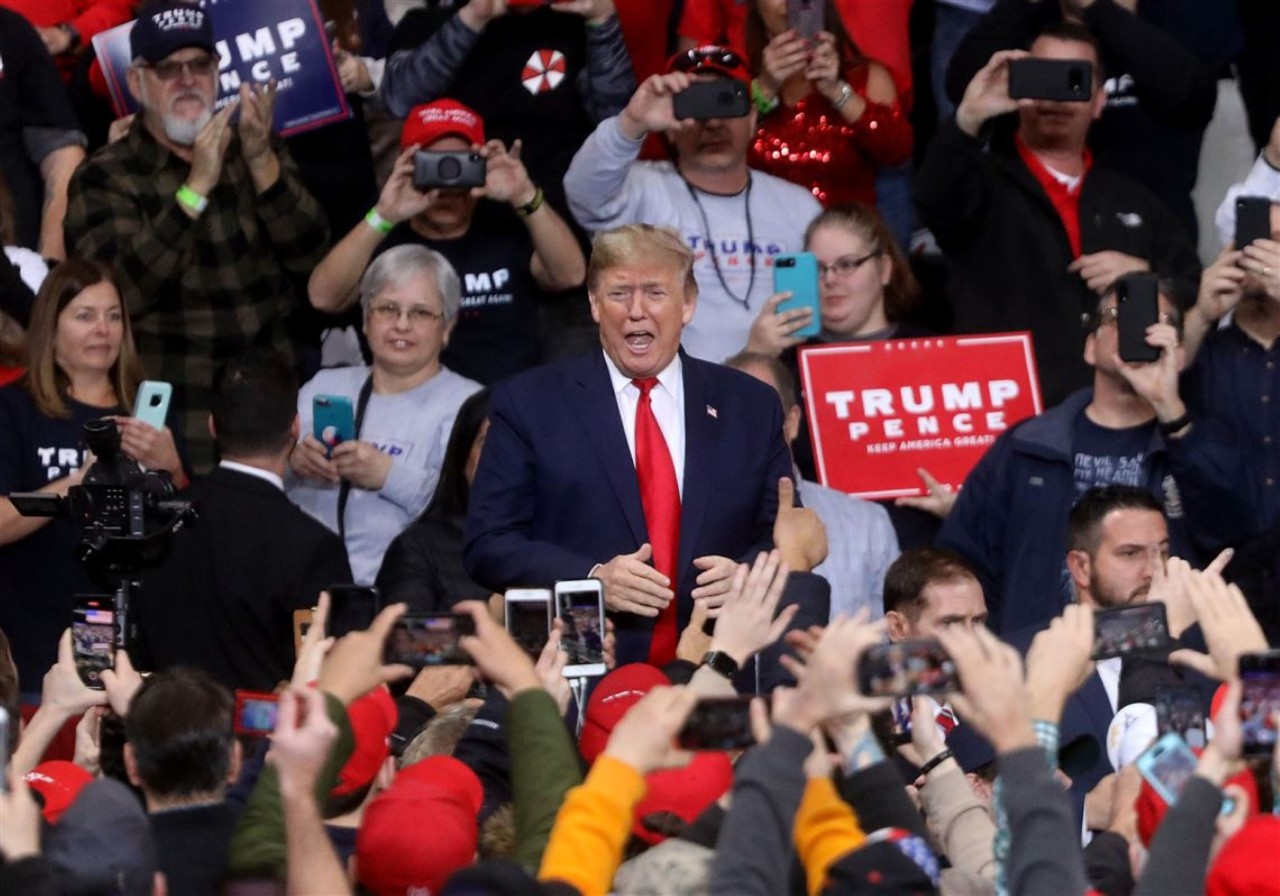 Donald Trump in the center of supporters waving Trump signs at a political rally.