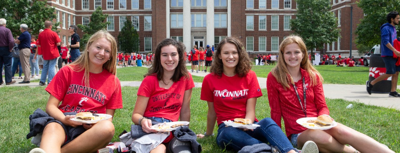 Four students sitting in the grass in front of Baldwin Hall at UC