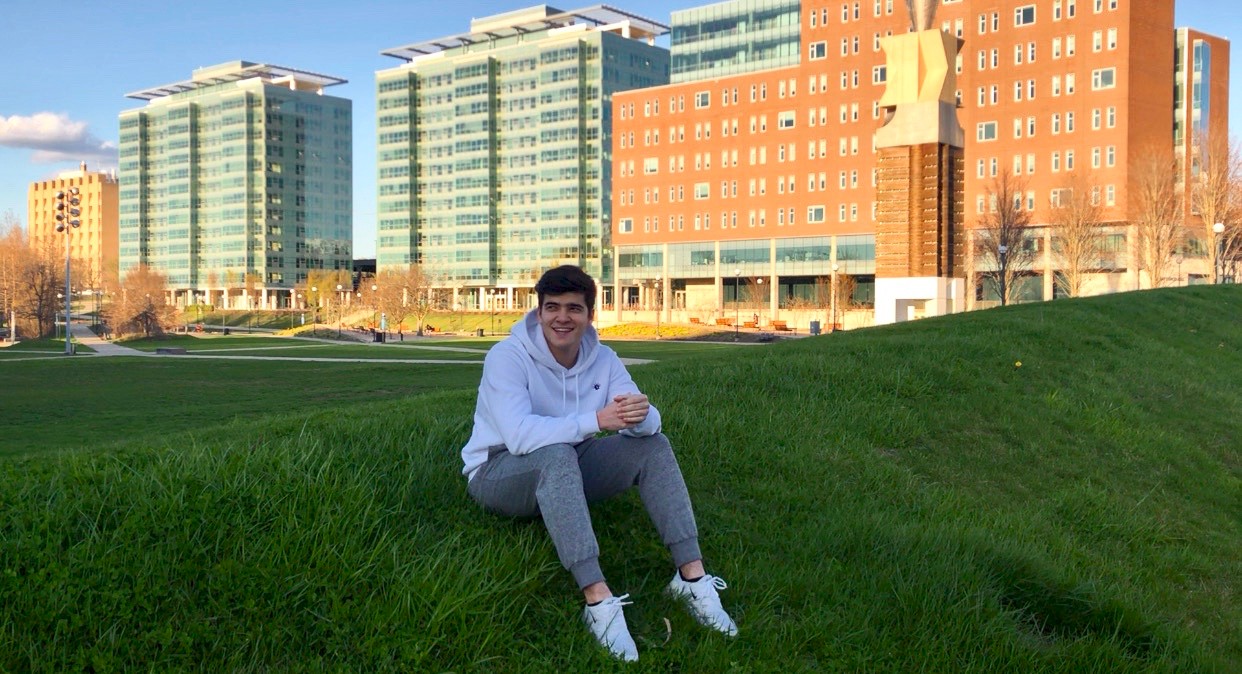 UC business student Komronbek Rakhimov sits on Sigma Sigma Commons in front of Marian Spencer Hall.