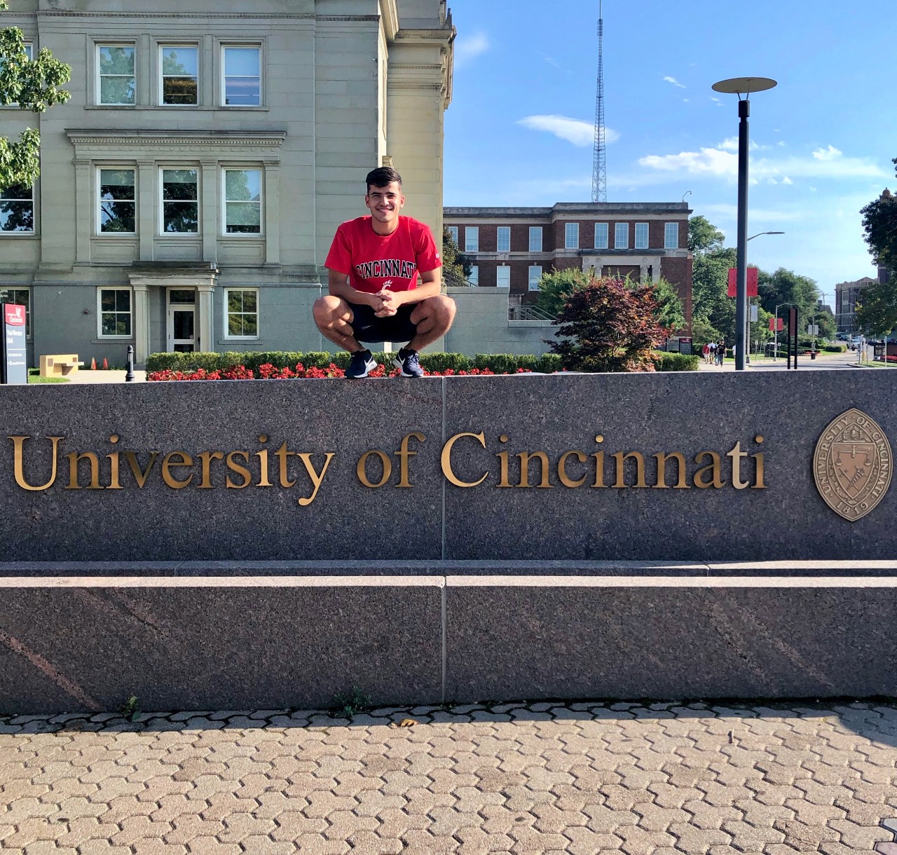 UC student Komronbek Rakhimov stands on top of UC's entrance sign.