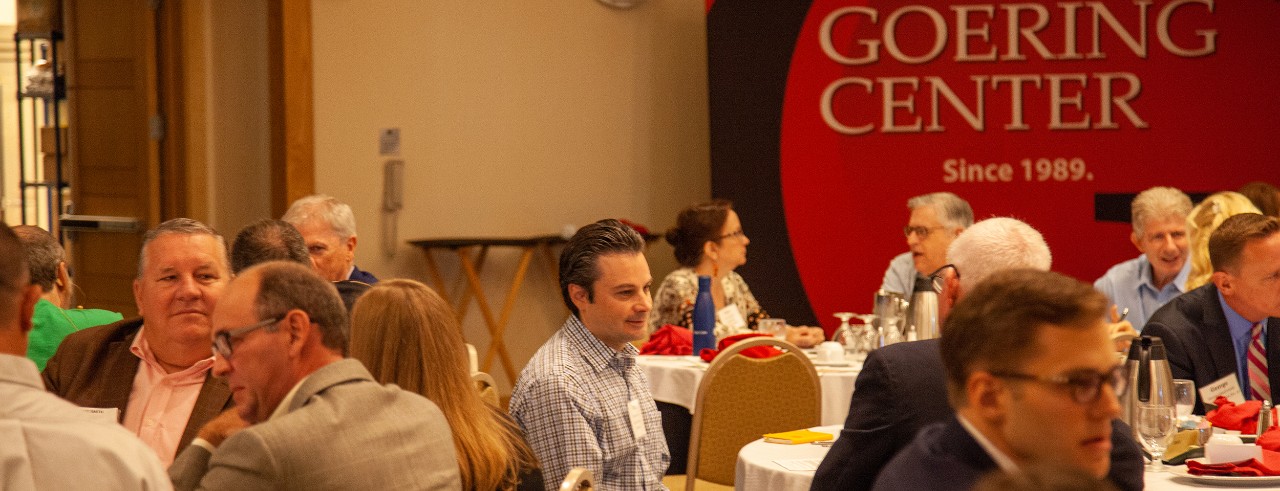 Attendees of Lift conference sitting down talking at tables with Goering Center banner in background.