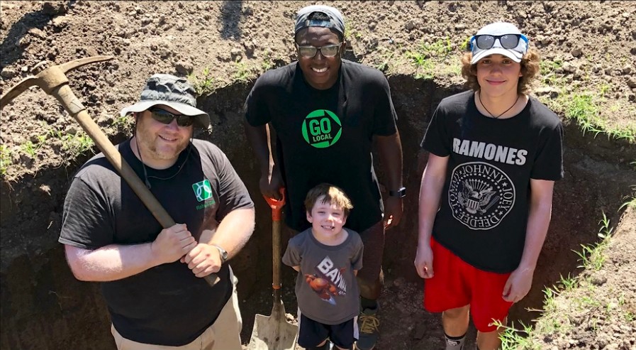 Three men and a child pose for a photo while digging a trench for a clean water line