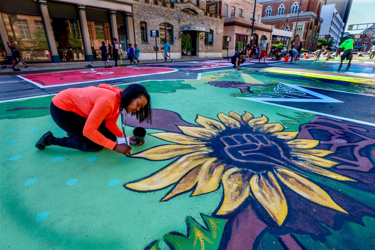 UC's Adoria Maxberry leans over painting her her street mural.