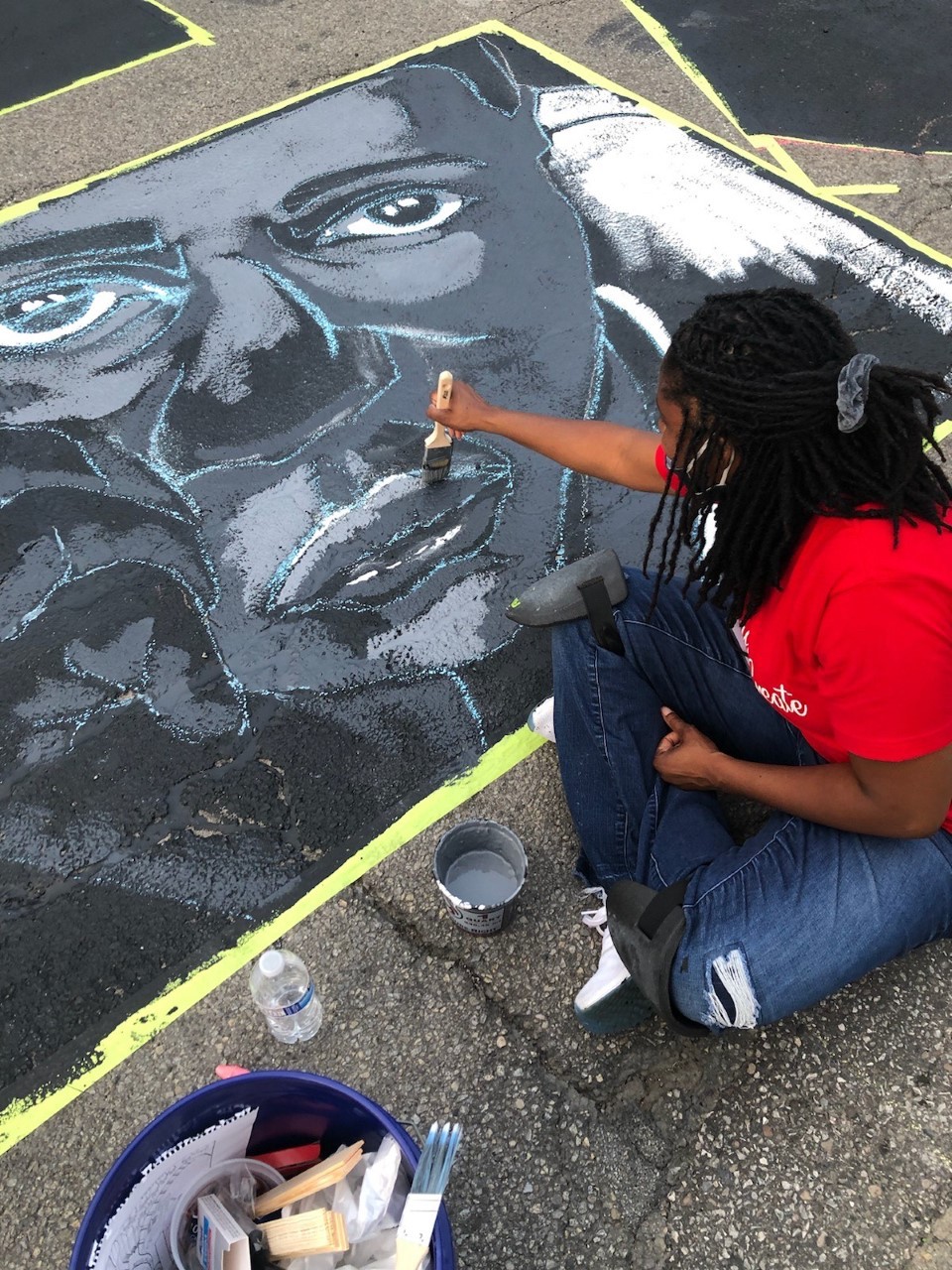 UC's Latausha Cox sits on the ground painting a figure in her street mural.