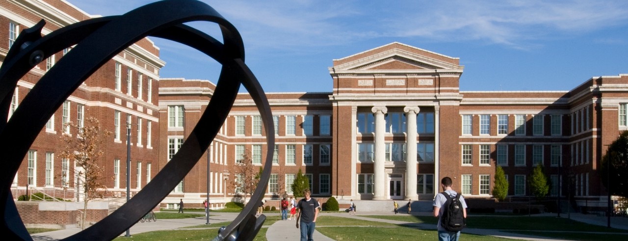 a daytime view of Baldwin hall, a light brick building with white columns, from the quad.