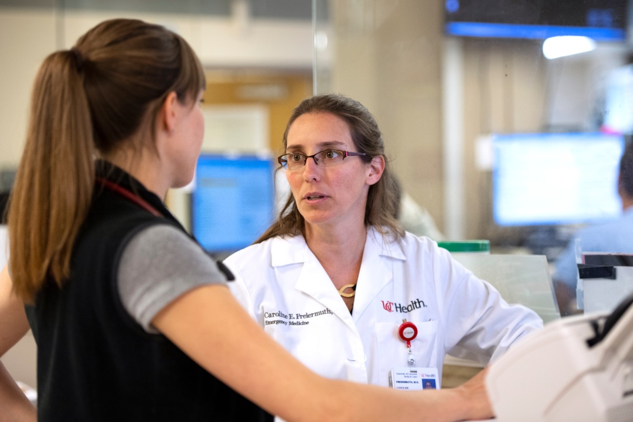 a woman doctor in a white lab coat talks to a colleague in a hospital emergency room