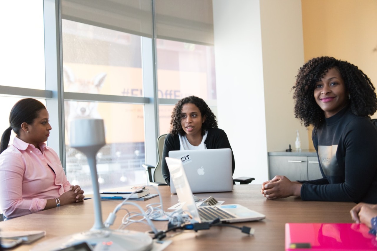 three black women sitting at a work station with computers.