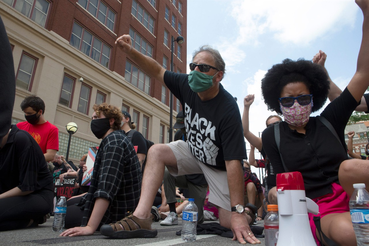 people kneeling on a Cincinnati street with their fists in the air during a protest march