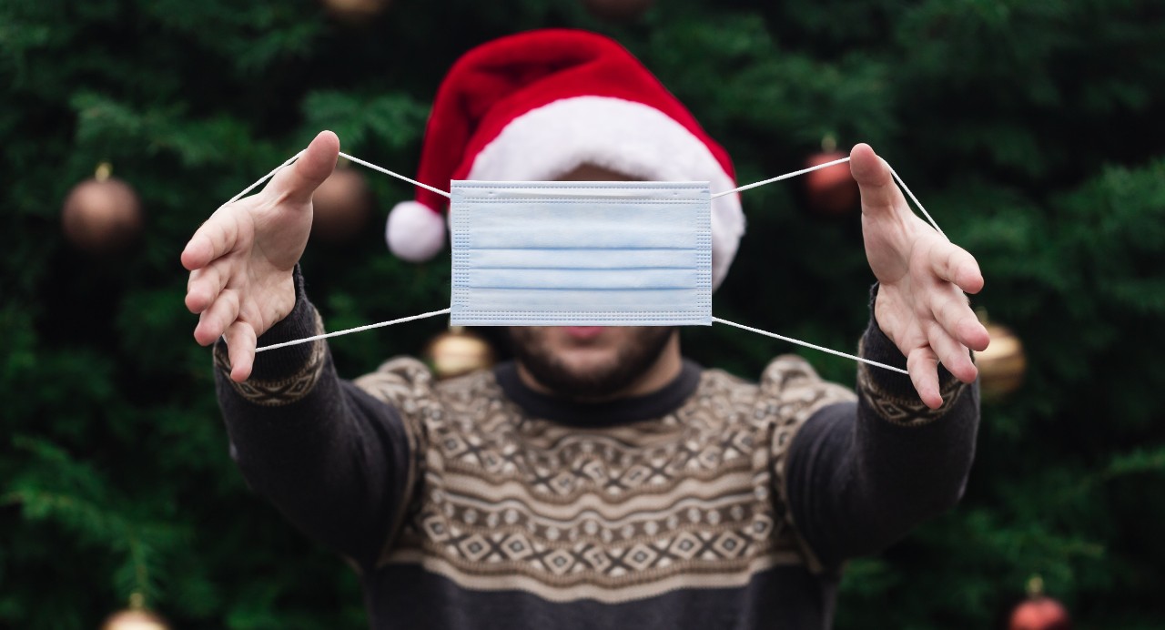 A man wearing a Santa hat stretching out a face mask in front of his face
