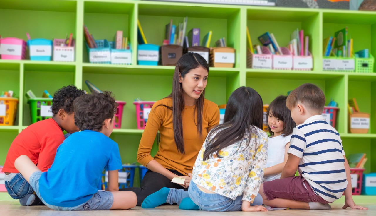 Kindergarten teacher with small group of mixed race children sitting on the floor 
