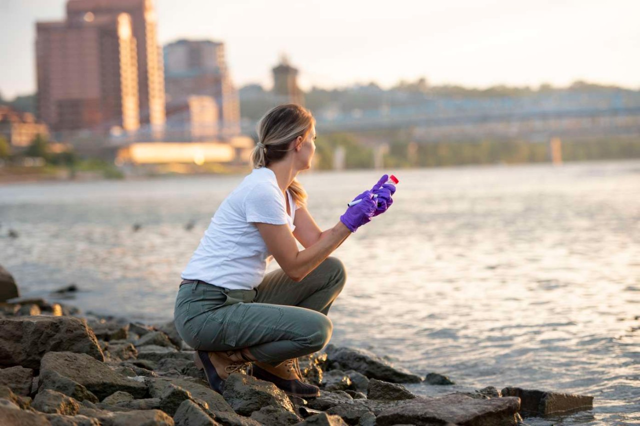 A UC student takes a water sample from a river.