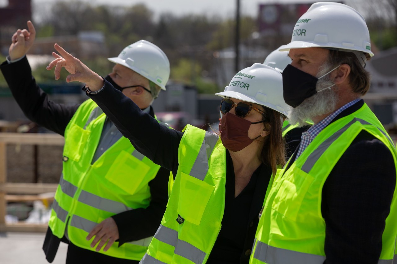 Three people in hardhats and safety vests gesture to the sky.