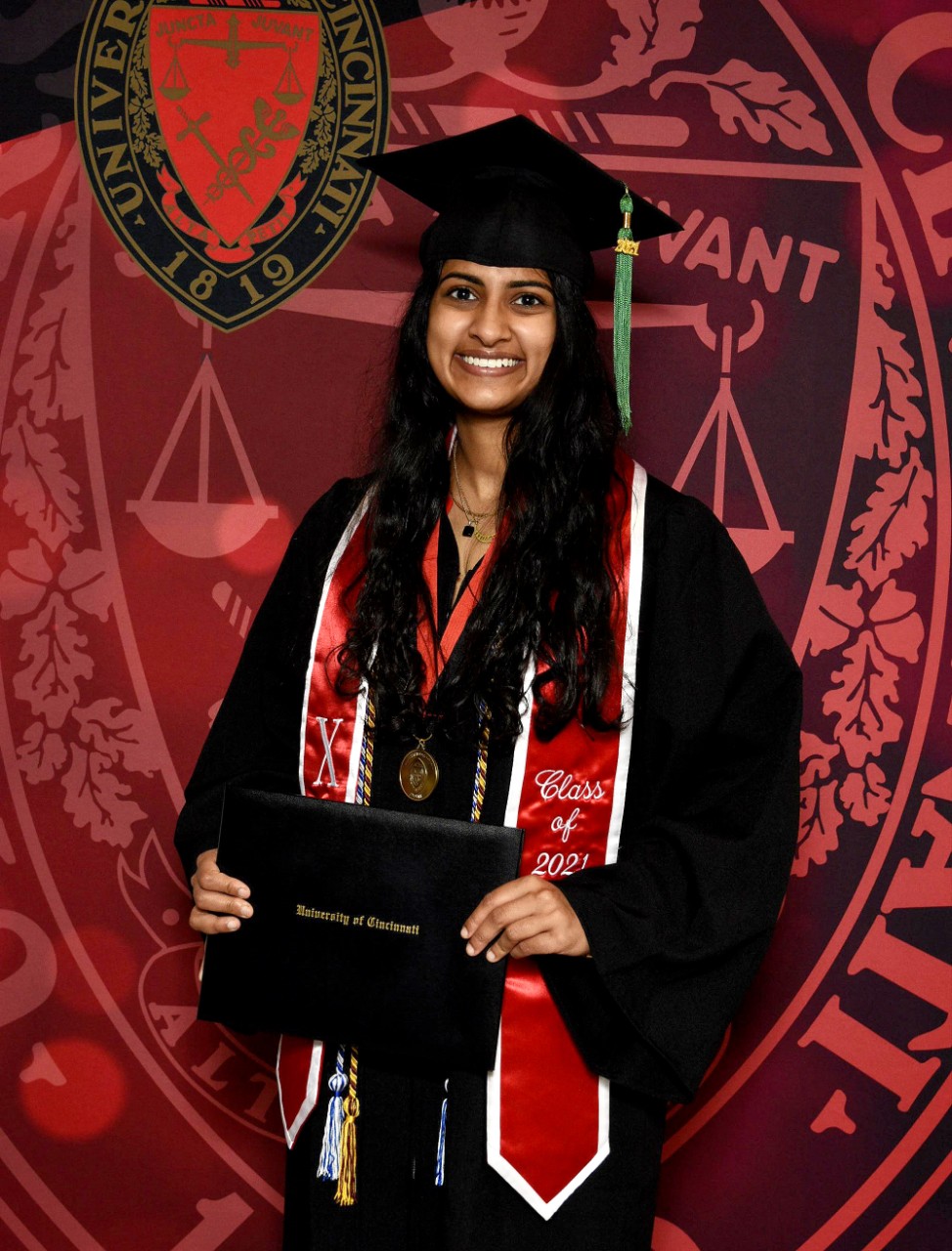 UC's Priyanka Vemuru wearing a UC graduation cap and gown holding her diploma.