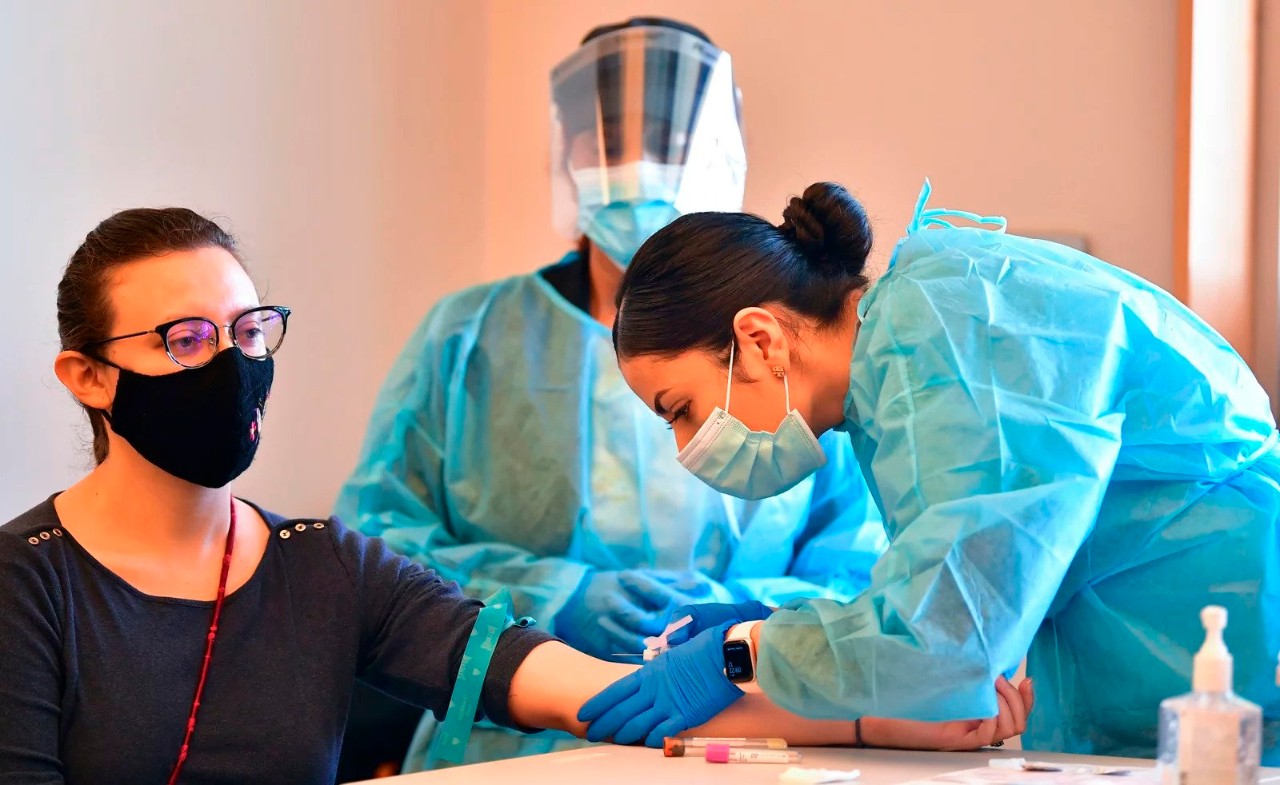 A phlebotomist draws blood from a patient at a COVID-19 antibody testing event