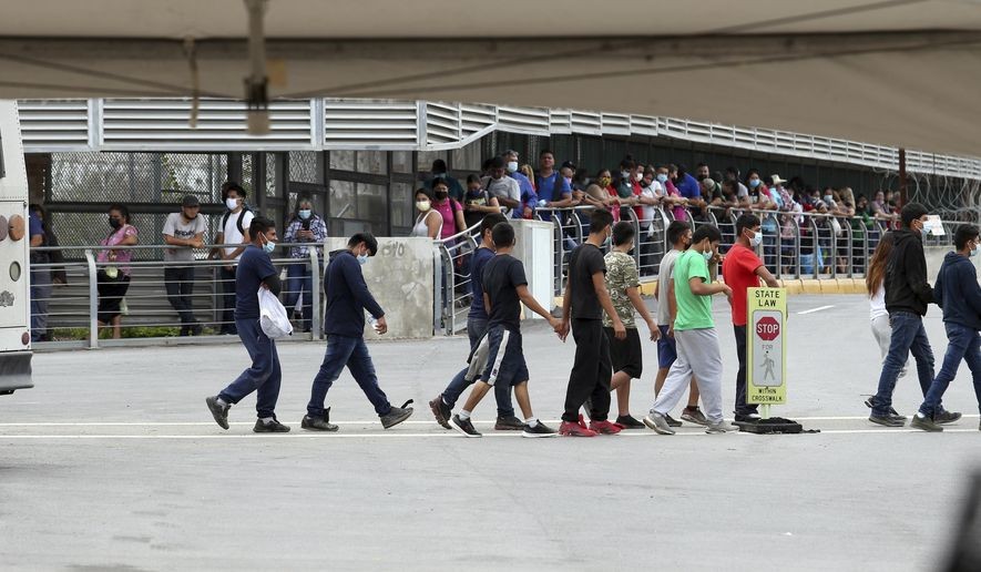 Immigrants wearing masks are escorted off an immigration bus in Hidalgo, Texas