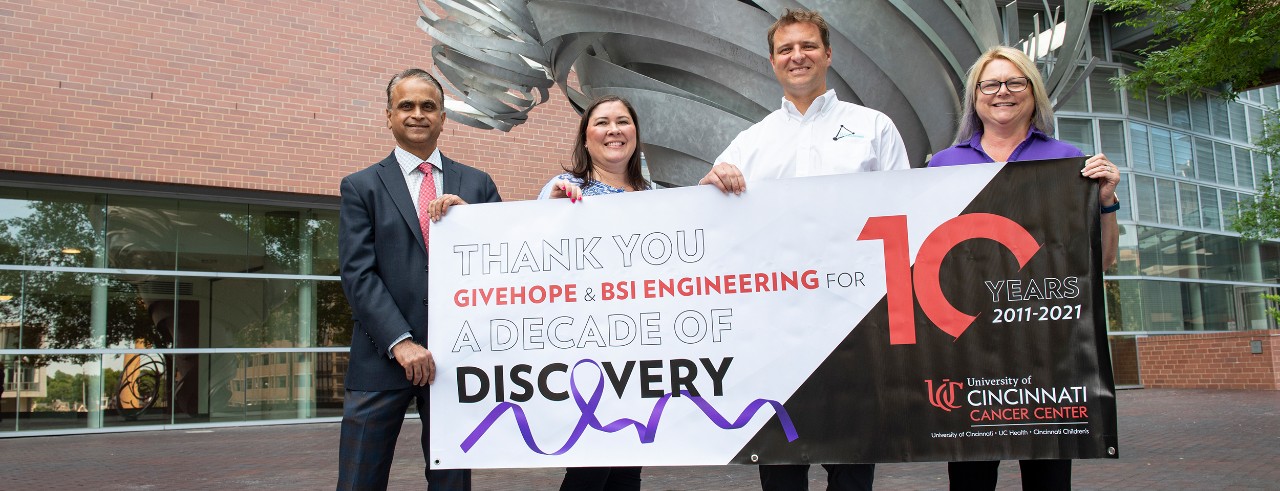 four people holding banner in front of UC College of Medicine. Two women and two men.