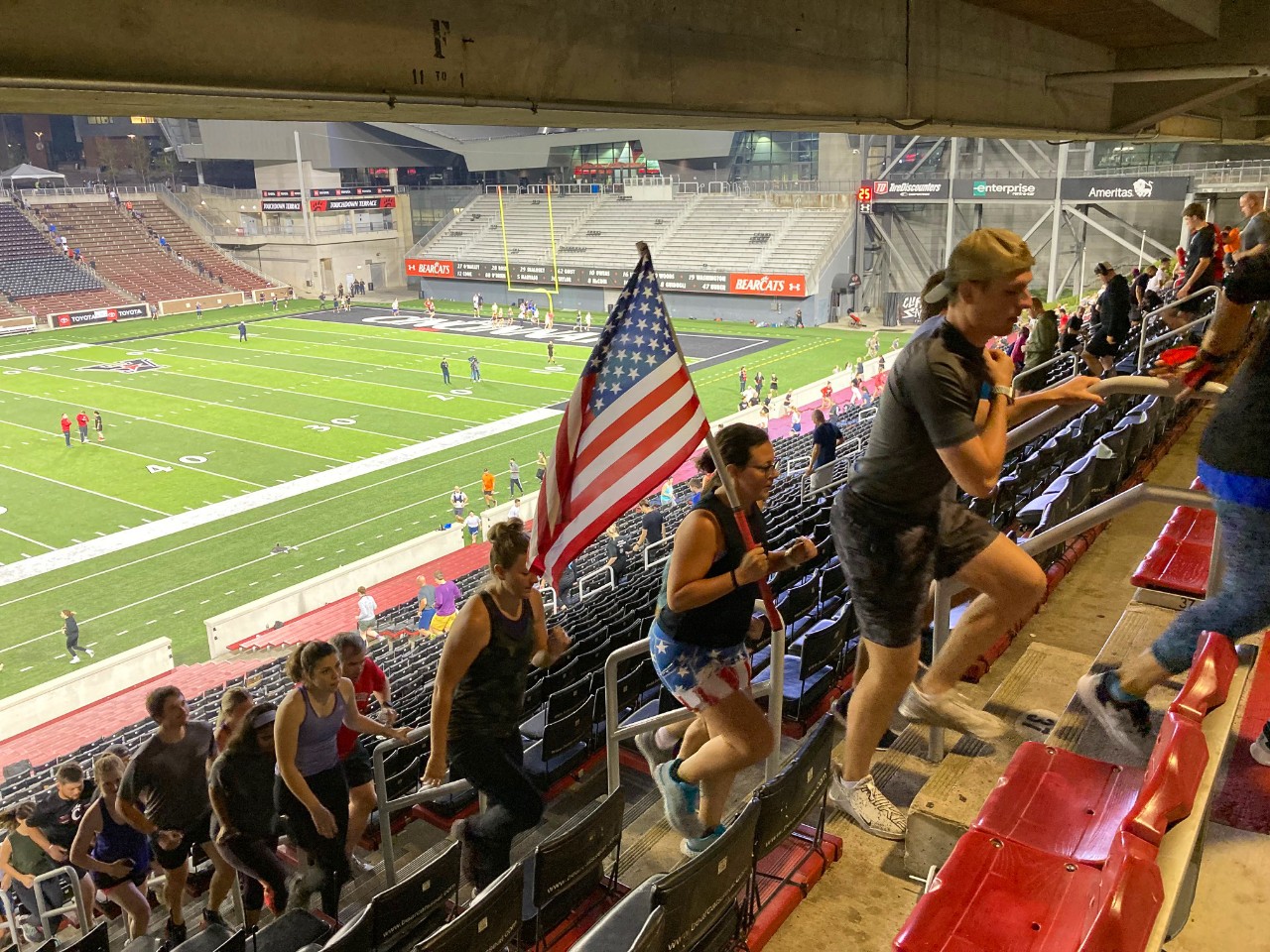 Students including one carrying an American flag run the steps of Nippert Stadium.