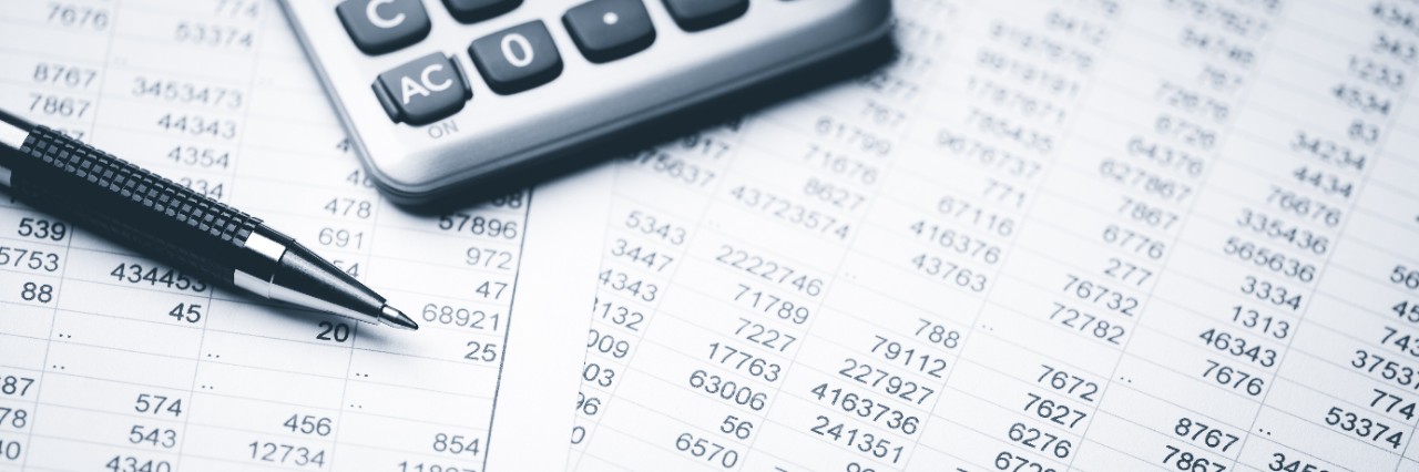 A pen and a calculator sit on top of paper with numbers.