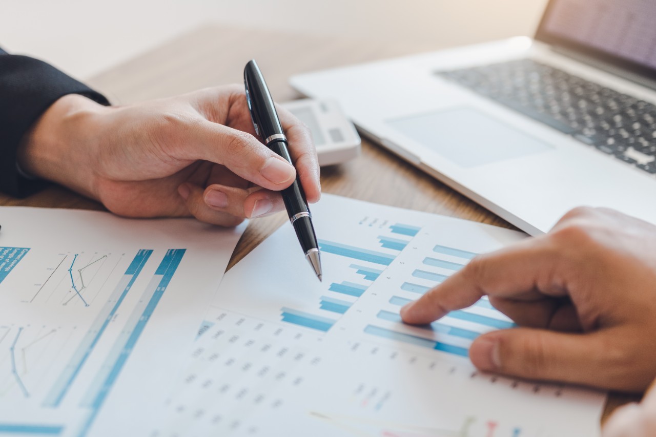 Two businessmen are pointing to the company cost graph and then analyzing together.