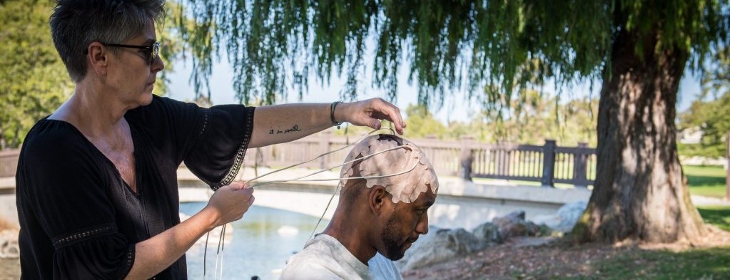 A woman applies electrical arrays to a male patient's head outdoors