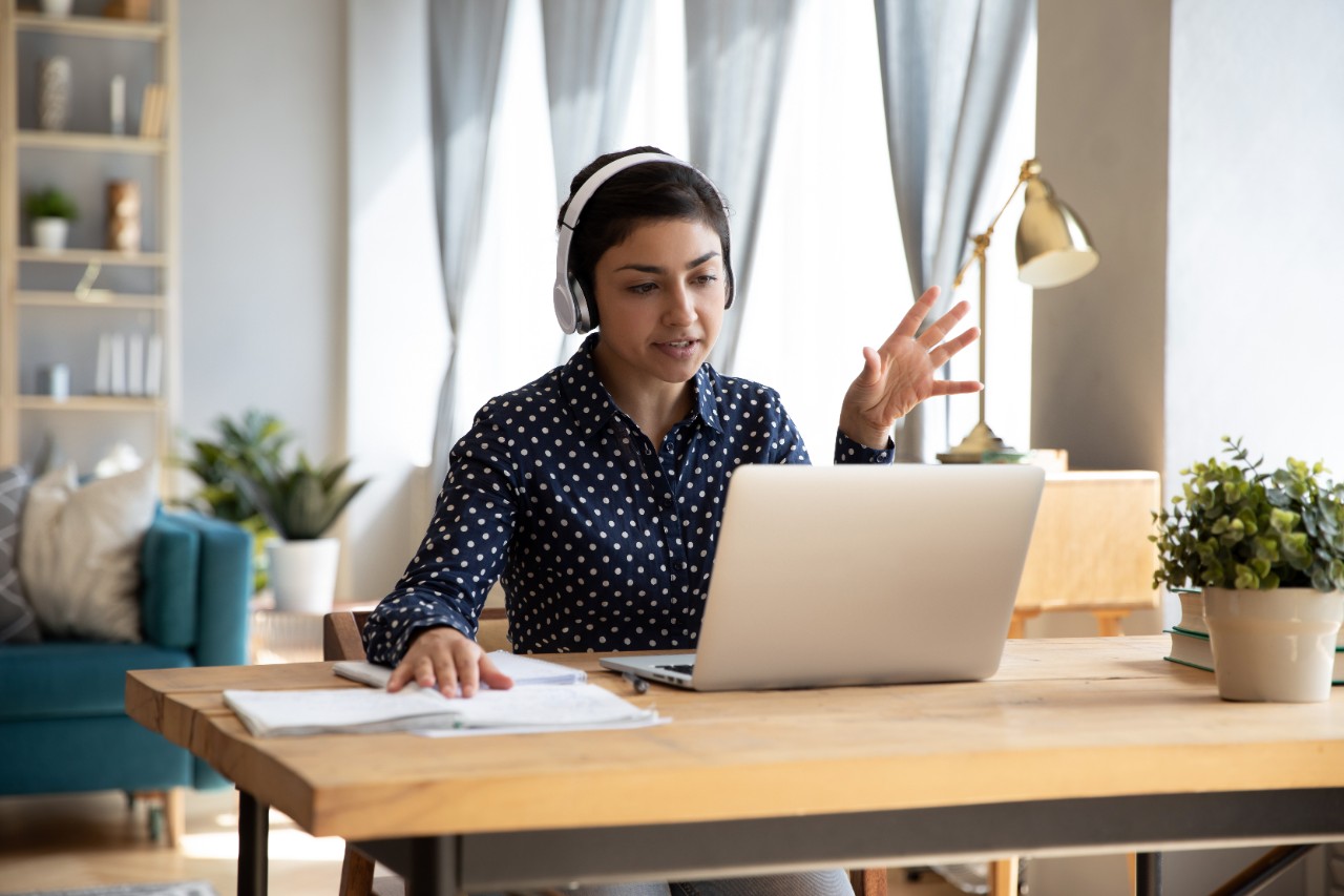 A woman employee in a blue shirt speaks on a video call from a remote work space.