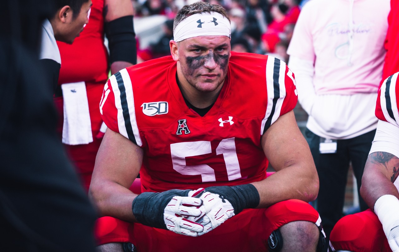 UC football player Lorenz Metz, in a red jersey, rests on the bench.