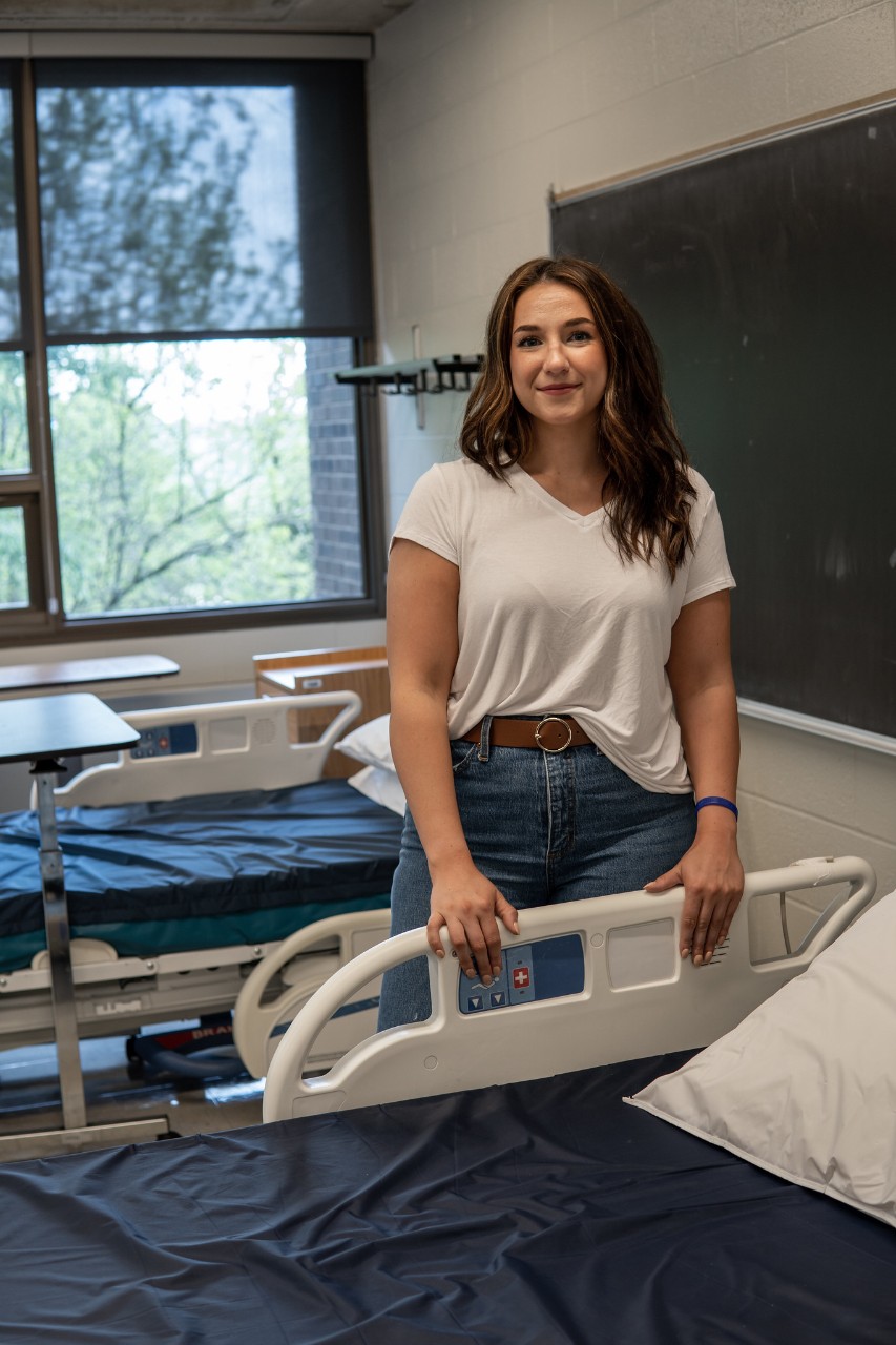 student standing by hospital bed in classroom