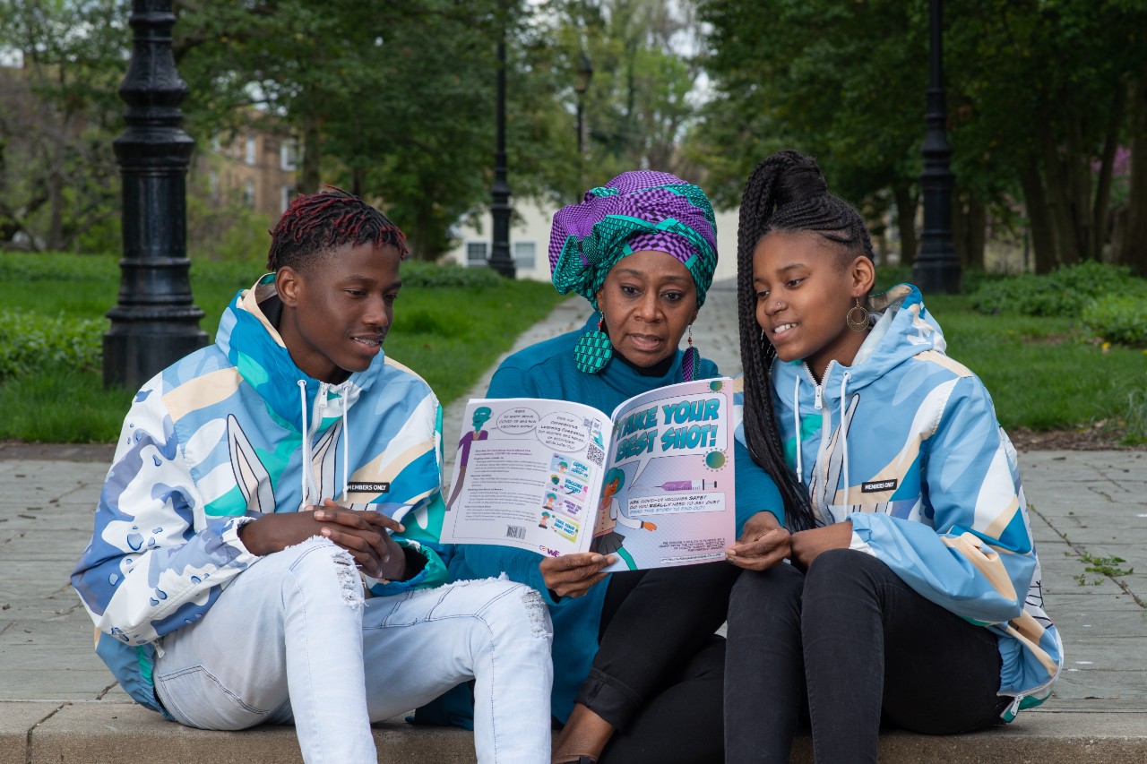 three people sitting in a park reading educational materials about COVID-19 vaccines
