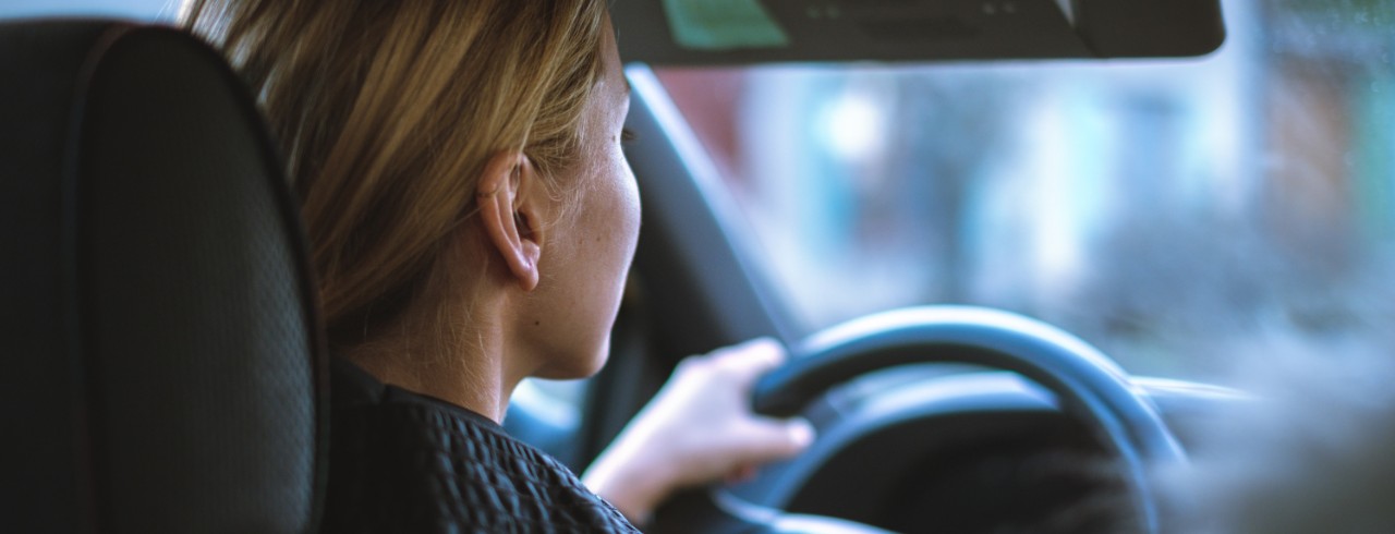 A young woman in the driver's seat of a car with her hands on the steering wheel