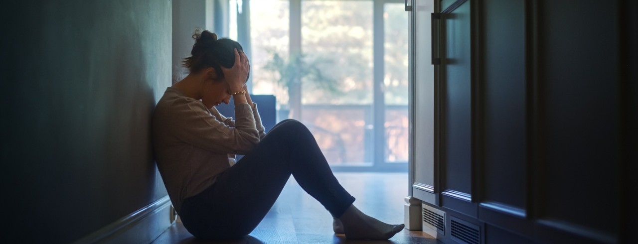 A woman sits on the floor with her head in her hands
