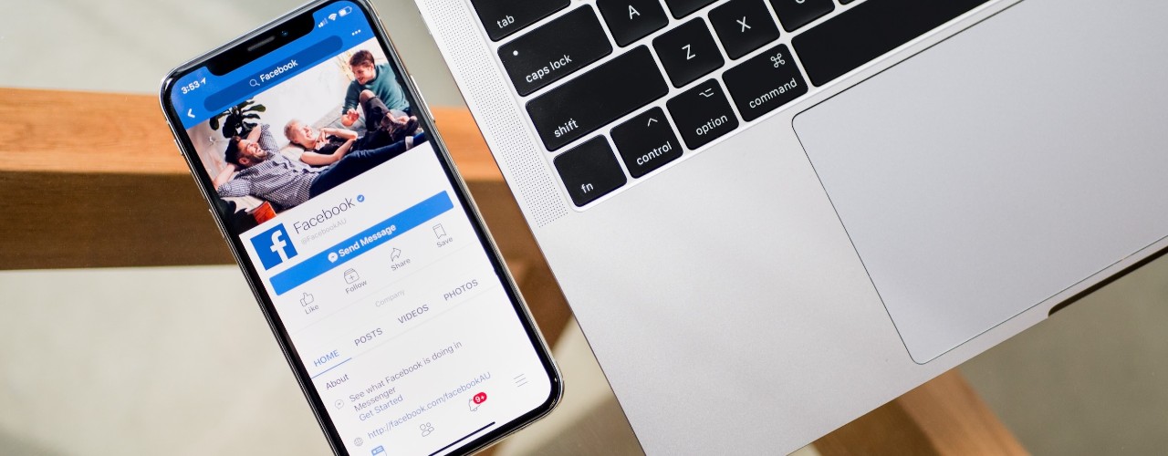 Cell phone on left showing the Facebook page and a laptop keyboard on right.