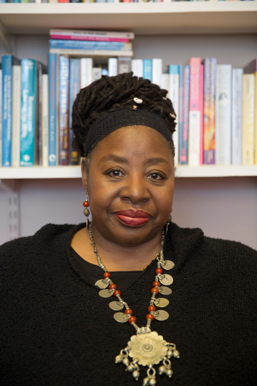Award-winning scholar, activist Loretta Ross wearing a gold necklace in front of a bookshelf