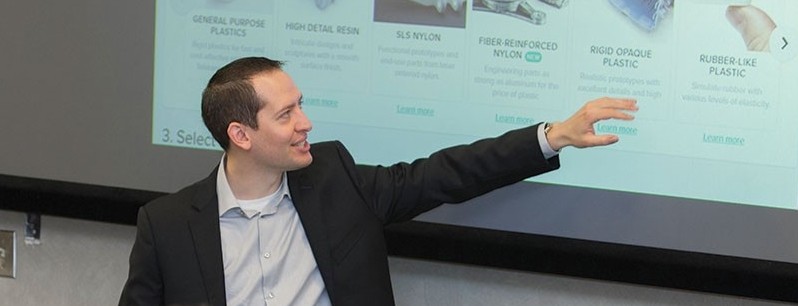 Lindner professor Elliott Manzon stands in front of a projector screen in front of a class of students
