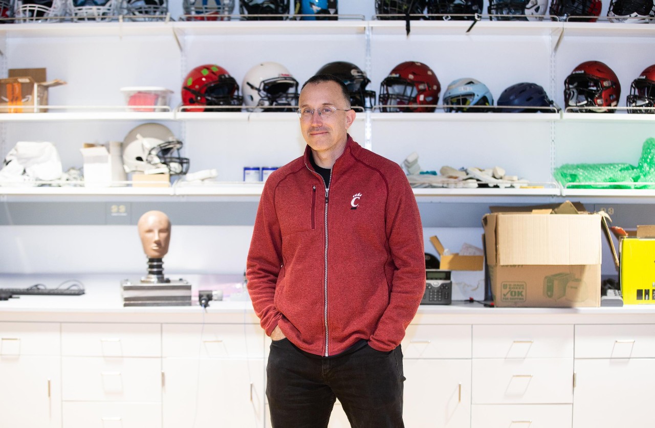 Eric Naumann stands against shelves holding football helmets.