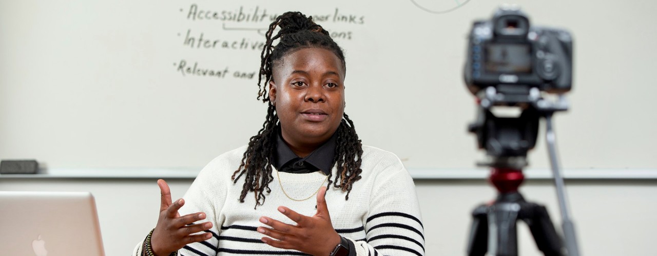 A woman looks into camera at virtual meeting in UC's 1819 Innovation Hub.