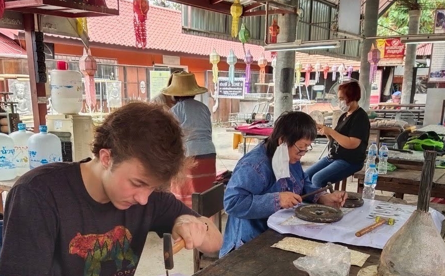 UC DAAP student Sam Pogue hammers a pattern into aluminum and sits next to Master Thoo, who is also hammering aluminum.