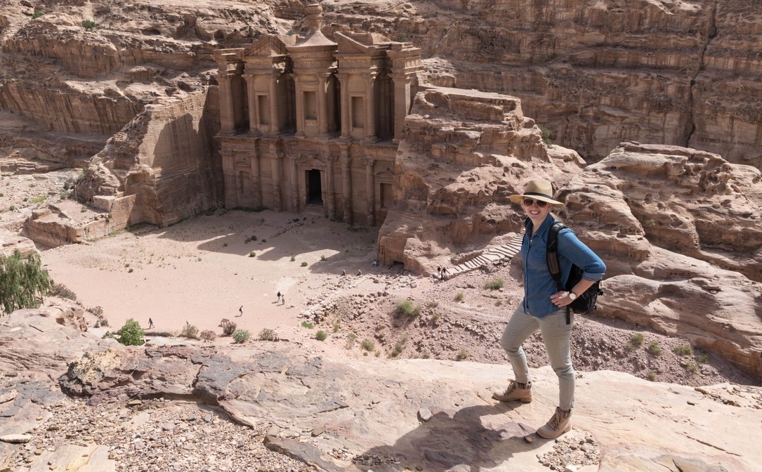 Sarah Wenner stands on a rock outcrop overlooking the carved clifftop façade of ancient Petra. 