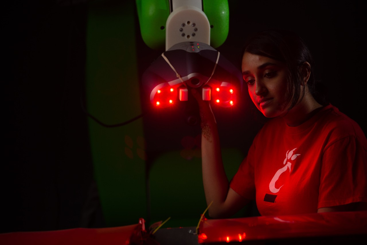 A student uses a laser device attached to a robotic arm.