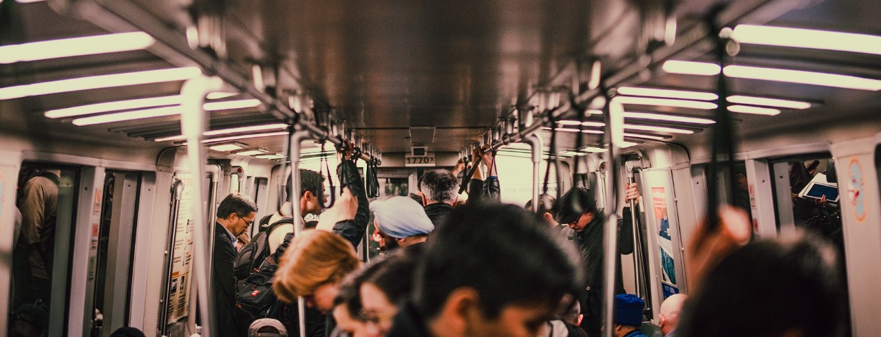 A crowd of people aboard a train stand and hold on to overhead railings