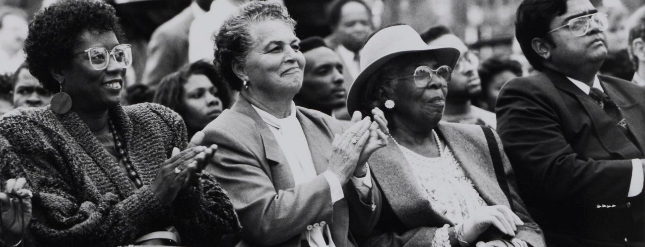 Marian Spencer is seat between two women on other side and she is applauding a speaker
