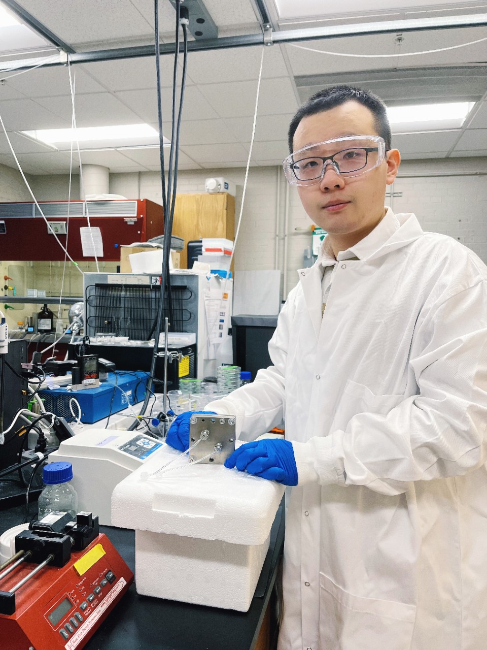 Zhengyuan Li in a labcoat and gloves works in a chemical engineering lab.
