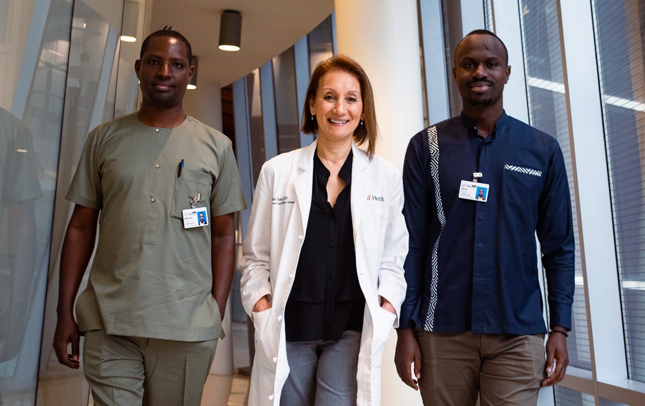 The three pose in a corridor ; Kerr is wearing a lab coat with her name and UC Health, while Muvunyi and Niyigena wear UC Health badges.