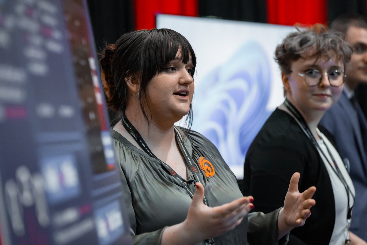 A woman explains her team's project while another woman looks at her.