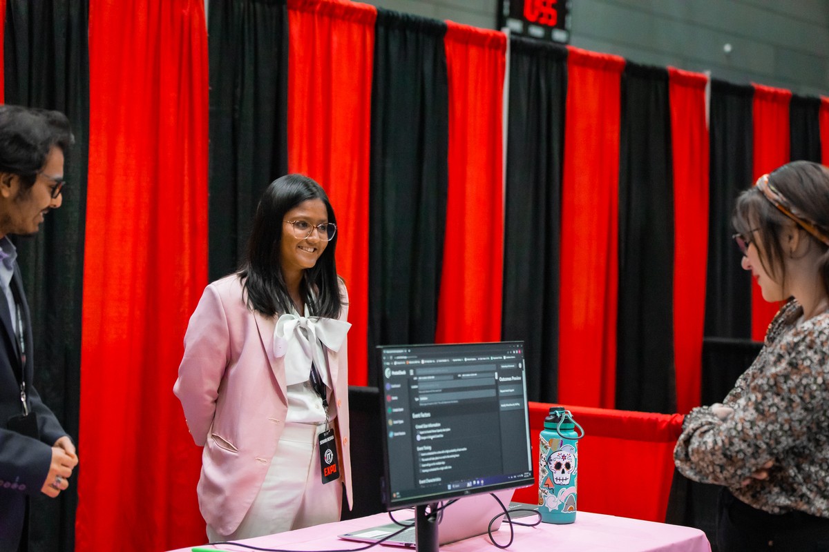 A woman stands behind a computer screen that another woman is looking at.