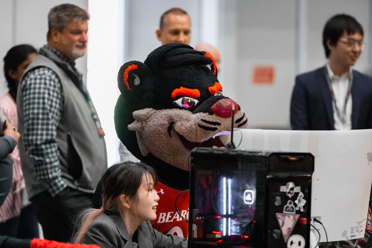 A student and the UC mascot look at a computer screen.